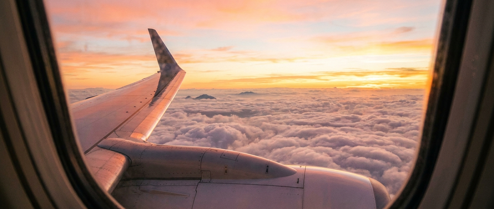 Aircraft wing above clouds at sunrise, representing the connecting flights and transits that decide yellow fever certificate rules